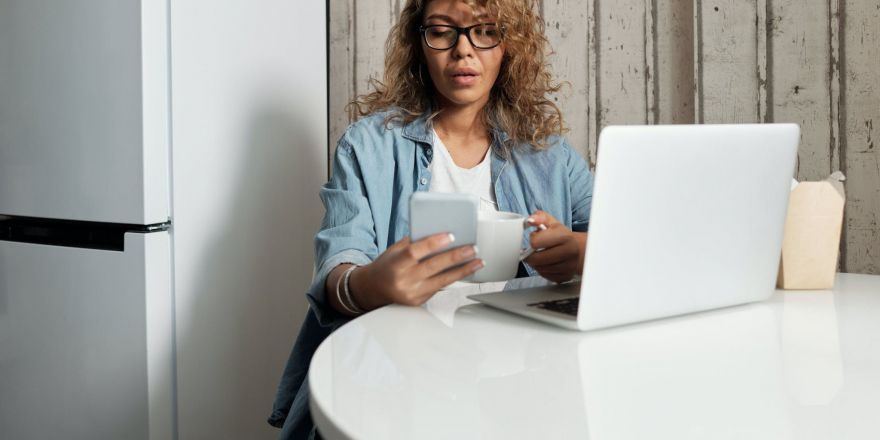 Vrouw achter laptop met mobiel in haar hand