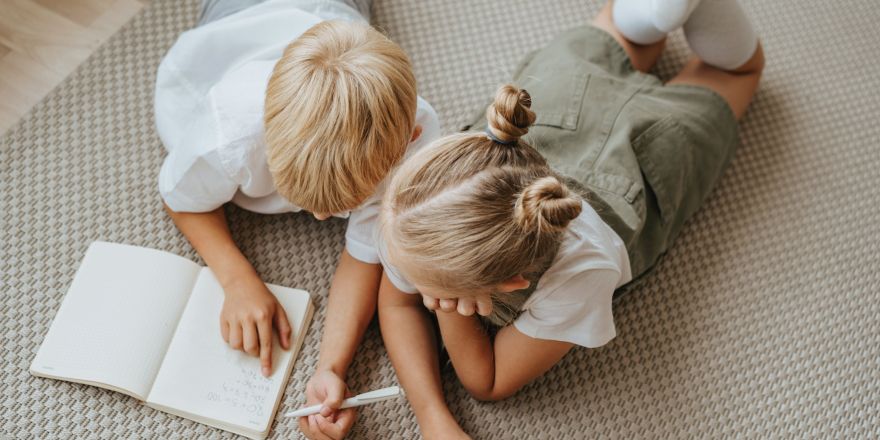 Een jongen en een meisje liggen op de grond met een schriftje