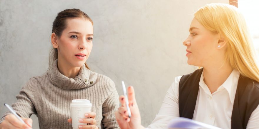 Twee vrouwen praten zittend aan een tafel