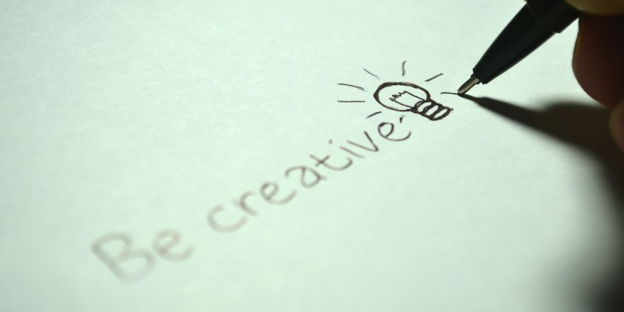 Hand schrijft 'be creative' op papier