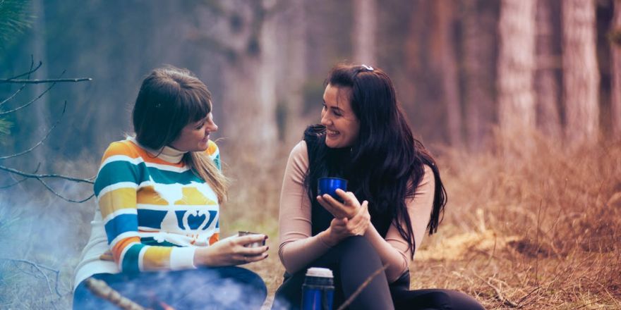 twee vrouwen praten met elkaar zittend in het bos bij een vuurtje