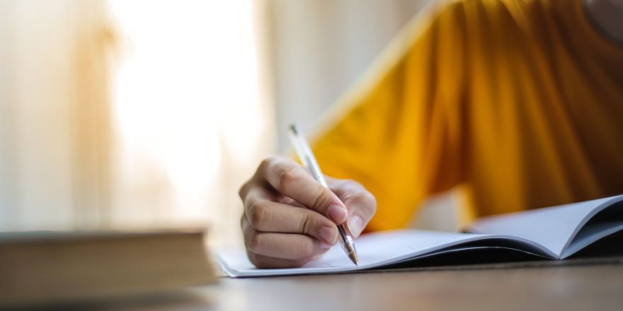 Persoon in geel shirt schrijft in notitieboek