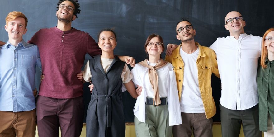 Diverse groep van 7 mensen staan arm in arm voor een muur