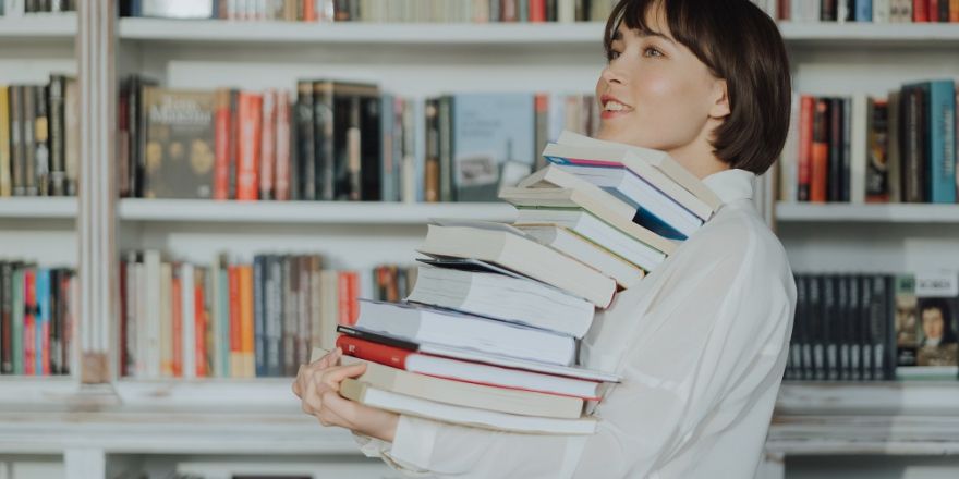 Vrouw draagt stapel boeken in de boekhandel