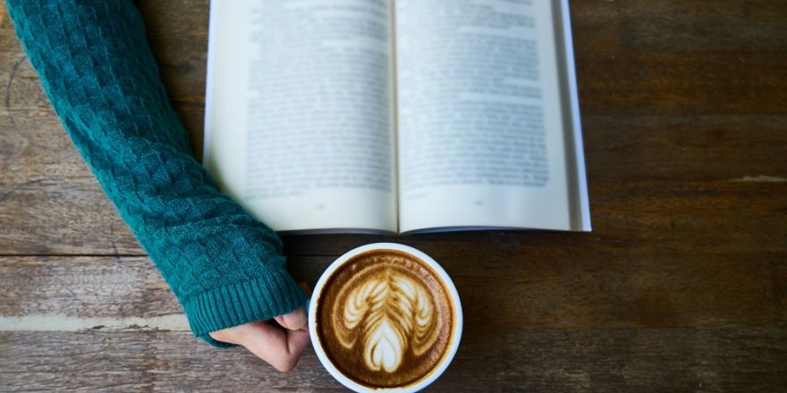 Persoon leest boek met kop koffie