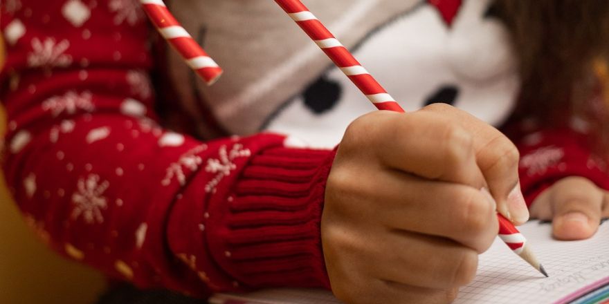 Vrouw met kersttrui schrijft in een notitieboekje met een pen in de vorm van een zuurstok