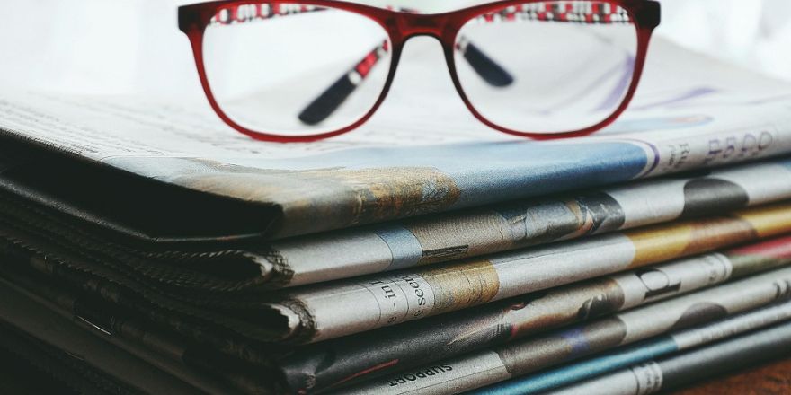 Afbeelding van een rode bril op een stapel kranten