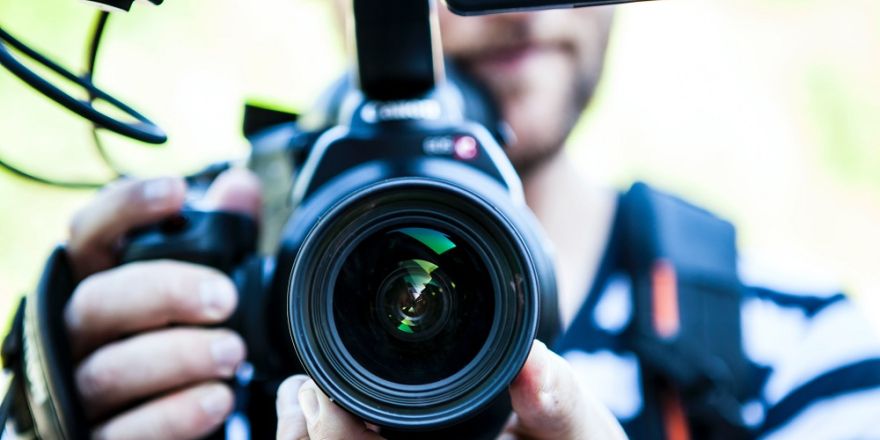 Grote afbeelding van een professionele nieuwscamera, cameraman erachter weinig in beeld