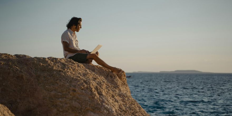 Man zit met laptop bij de zee