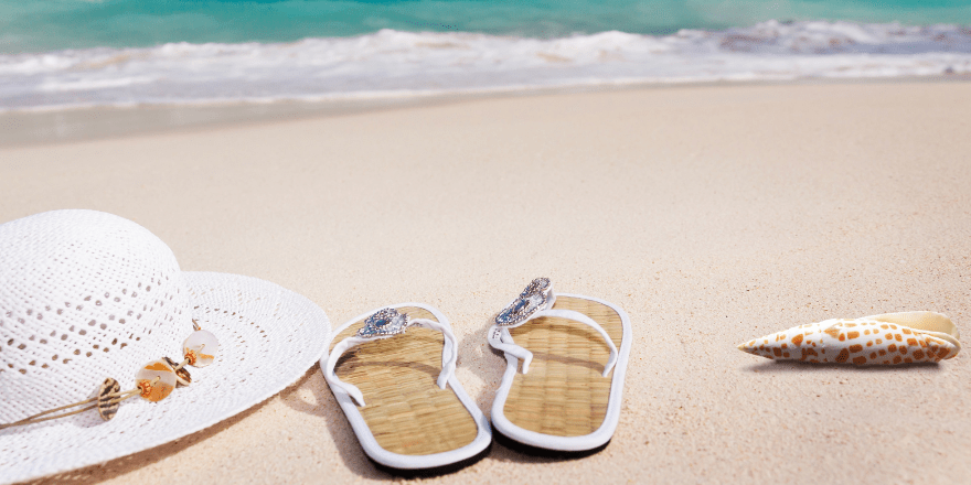 Hoed en teenslippers liggen op het strand