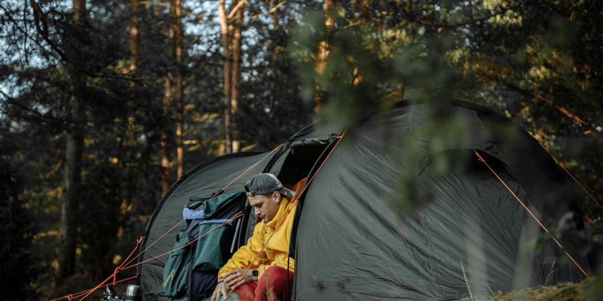 Persoon in oranje jas zittend op grijze tent in bos