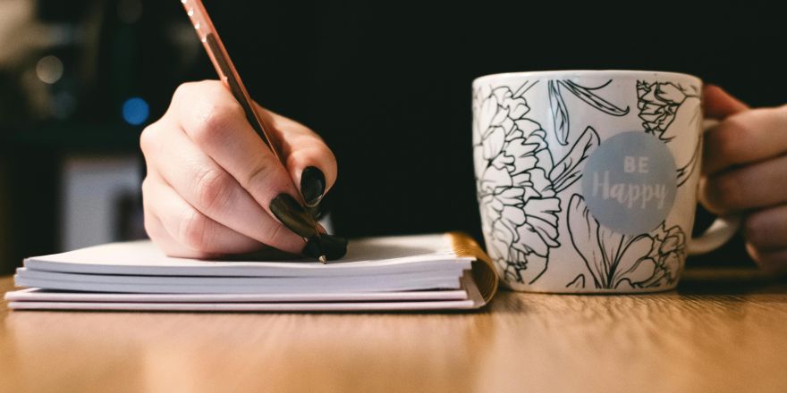hand met nagellak die schrijft en koffiemok vast heeft
