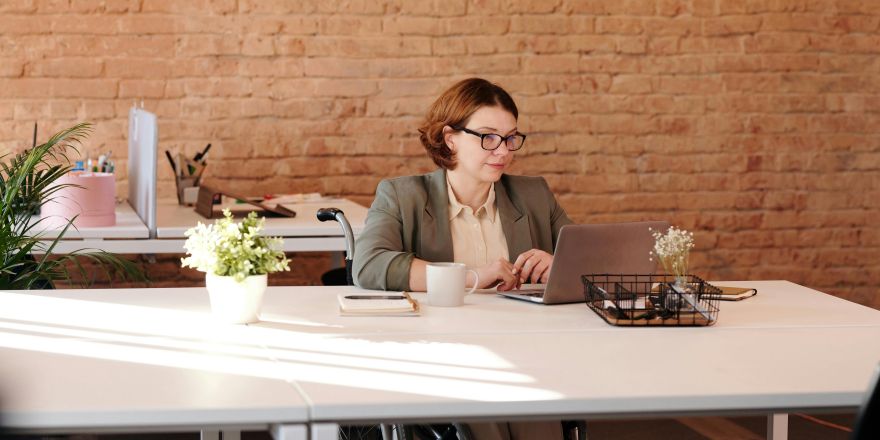 vrouw in rolstoel werkend aan bureau achter een computer