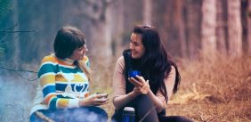 twee vrouwen praten met elkaar zittend in het bos bij een vuurtje