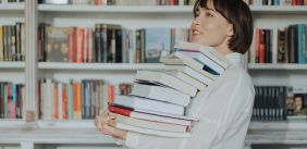 Vrouw draagt stapel boeken in de boekhandel