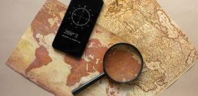 Een kaart van de Aarde en een andere wereldkaart, met daar bovenop een telefoon met de kompasapp en een vergrootglas.