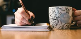 hand met nagellak die schrijft en koffiemok vast heeft