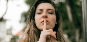 Vrouw houdt haar vinger tegen haar lippen in een stilte gebaar