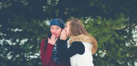 Vriendin fluistert vrouw een roddel in haar oor