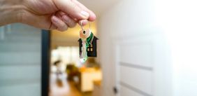 Hand houdt huissleutels vast voor een open deur