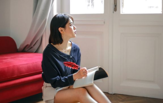 Vrouw in een kamer aan het schrijven met een veer in een schriftje