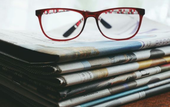 Afbeelding van een rode bril op een stapel kranten