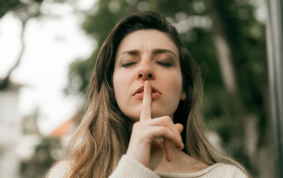 Vrouw houdt haar vinger tegen haar lippen in een stilte gebaar