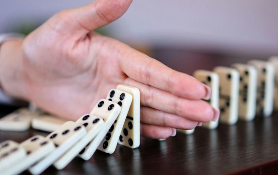 Hand tussen omvallende dominosteentjes
