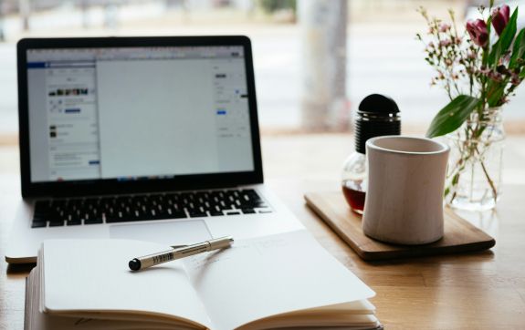 Laptop met open notebook ervoor en een kop ernaast