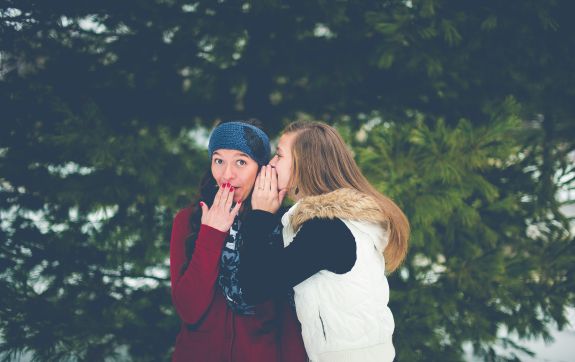 Vriendin fluistert vrouw een roddel in haar oor