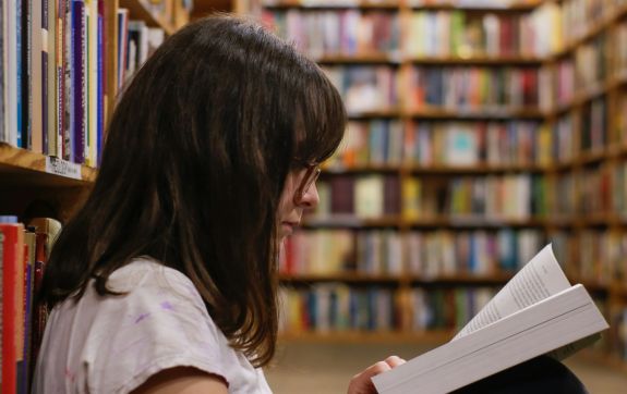 Tienermeisje leest boek in de bibliotheek