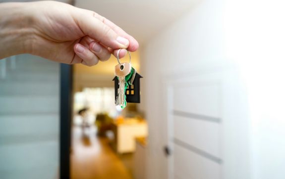 Hand houdt huissleutels vast voor een open deur